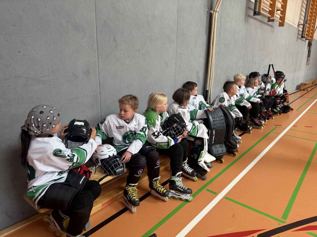 Pulheimer Bambini auf der Bank mit Helmen und Schienbeinschonern in der Sporthalle