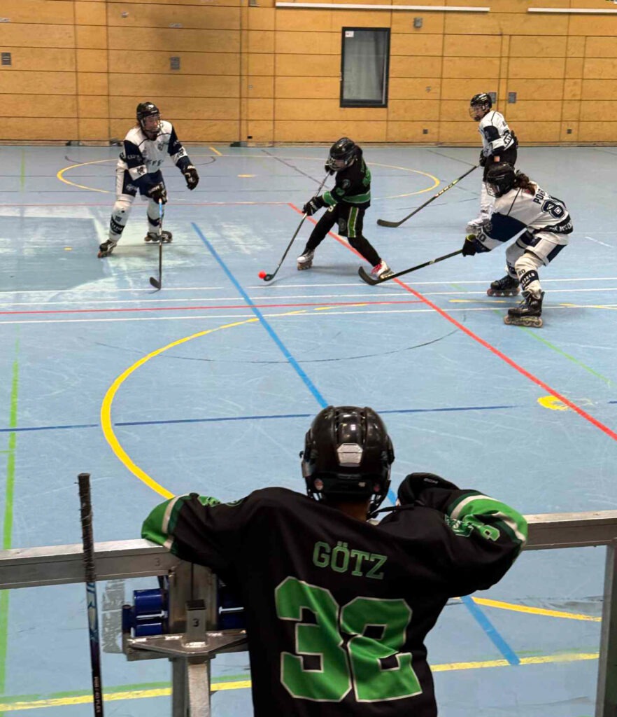 Inlinehockey-Spielszene mit Pulheim Vipers in weiß und grünem Gegner im Angriff auf dem Hallenboden